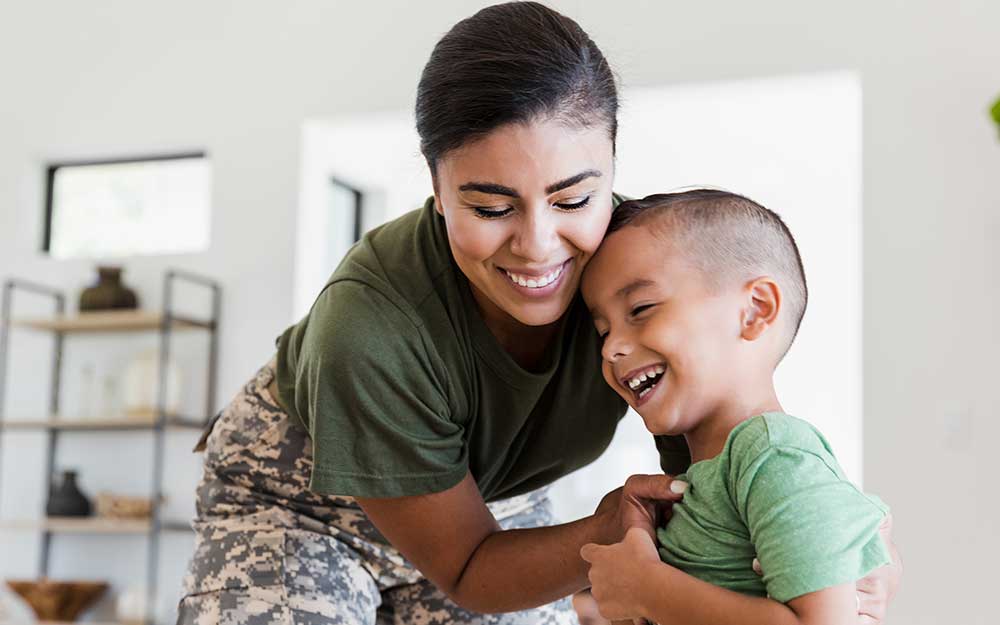 Woman in military uniform smiling and picking up her young son